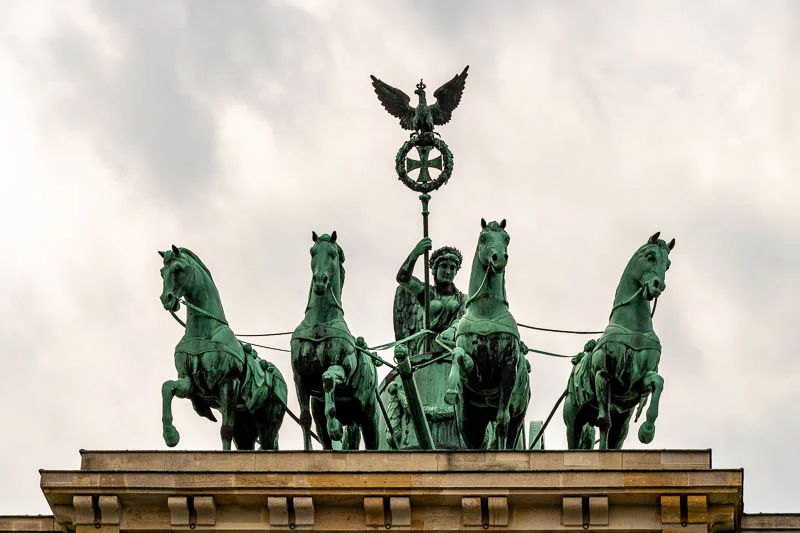 Quadriga auf dem Brandenburger Tor in Berlin bei bewölktem Himmel. Die bronzene Skulptur zeigt die Siegesgöttin Victoria in einem von vier Pferden gezogenen Streitwagen.