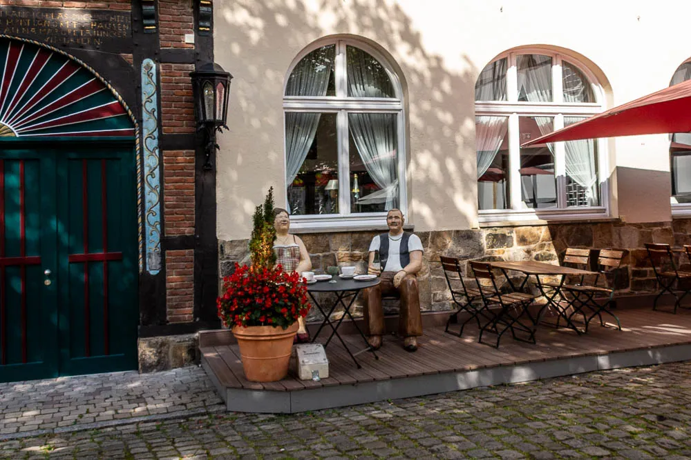 Zwei Figuren sitzen an einem kleinen Tisch vor einem Gebäude in Rheda-Wiedenbrück
