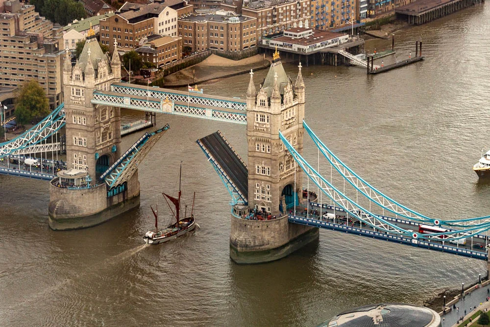 Geöffnete Tower Bridge in London mit einem Segelschiff auf der Themse.