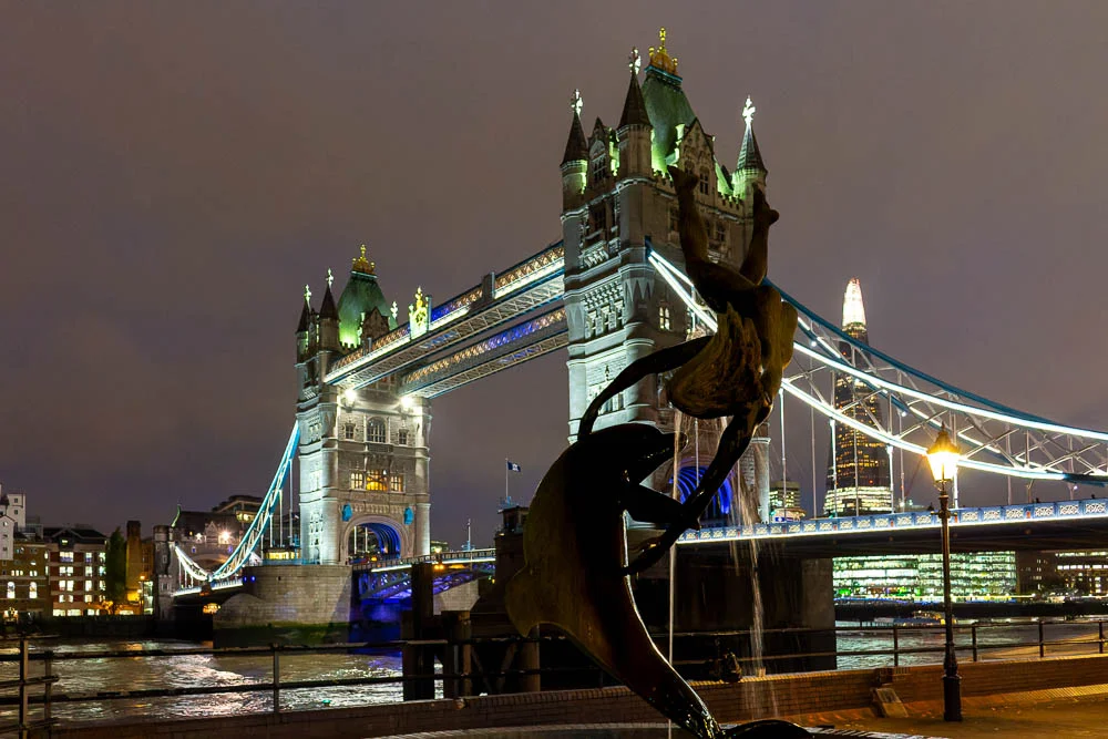 Tower Bridge bei Nacht mit der Skulptur „Girl with a Dolphin“ im Vordergrund.