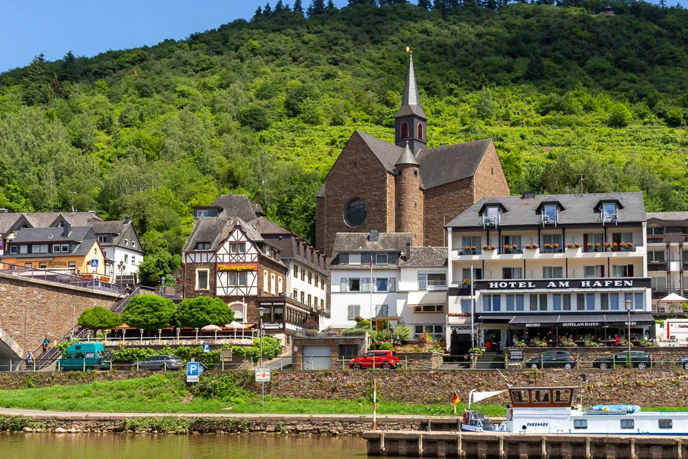 Ort an der Mosel mit Kirche, Hotels und Weinbergen am steilen Hang.