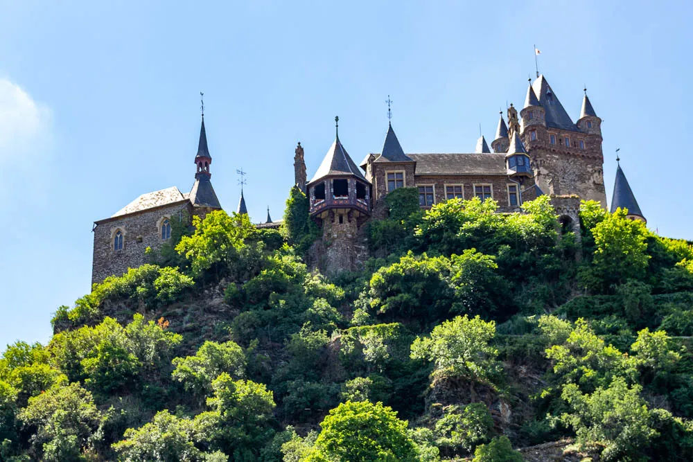 Reichsburg Cochem auf einem bewaldeten Hügel über der Mosel, vom Schiff aus fotografiert.