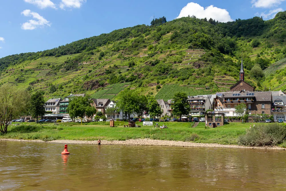 Blick vom Schiff auf den Moselort Valwig mit Kirche und steilen Weinbergen.