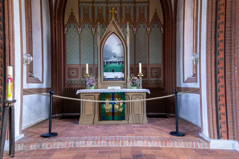 Der Altar der Inselkirche Langeoog mit farbig gestaltetem Hintergrund, Kerzen und Blumen.