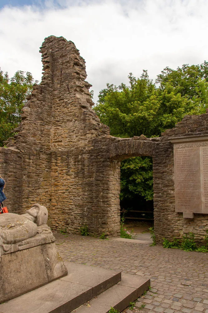 Ein Torbogen und erhaltene Mauern der Burgruine Hohensyburg stehen neben einer Gedenktafel.