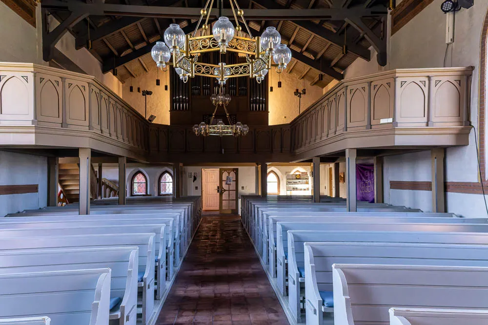 Blick durch den Innenraum der Inselkirche Langeoog auf die Empore mit der Orgel und den Kirchenbänken.