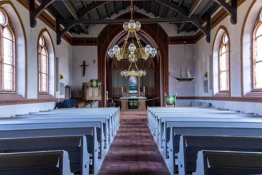 Blick durch den Innenraum der Inselkirche Langeoog auf Altar und Kanzel mit den Kirchenbänken im Vordergrund.