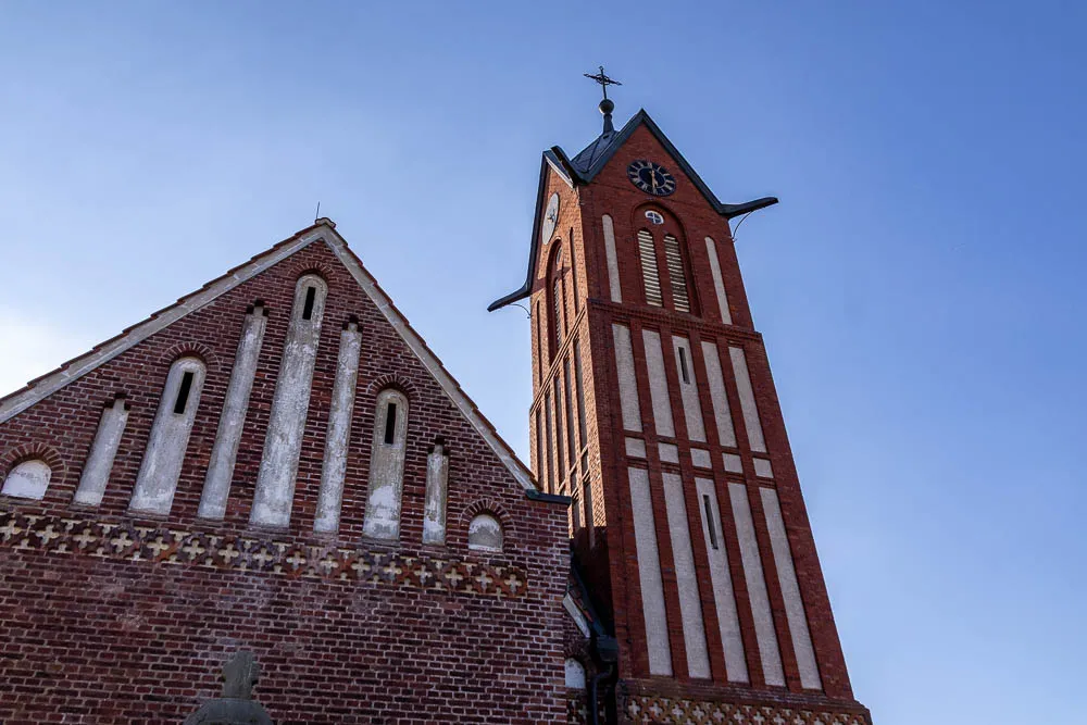 Blick von unten auf den Kirchturm und die Backsteinfassade der Inselkirche Langeoog vor blauem Himmel.
