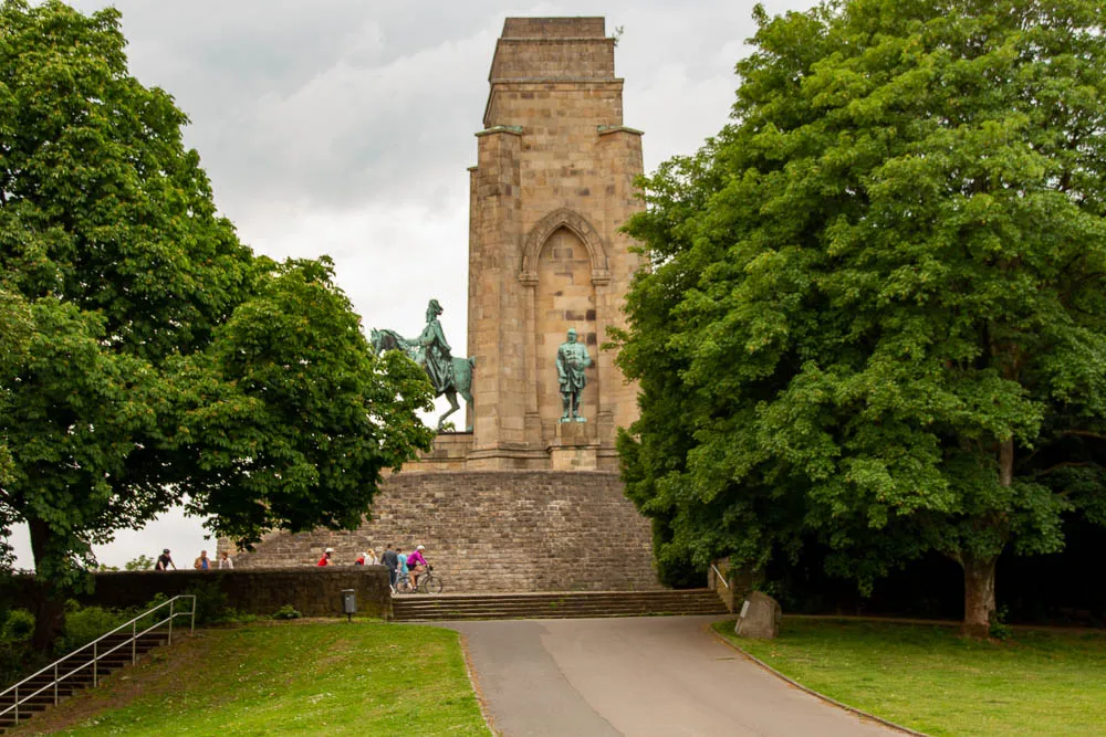 Das Kaiser-Wilhelm-Denkmal auf der Hohensyburg steht zwischen Bäumen vor einem bewölkten Himmel.