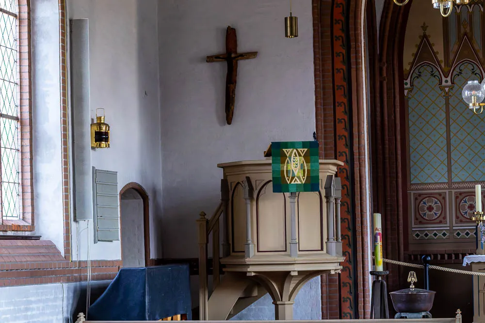 Die Kanzel der Inselkirche Langeoog mit einem Holzkreuz an der Wand und Blick zum Altarraum.
