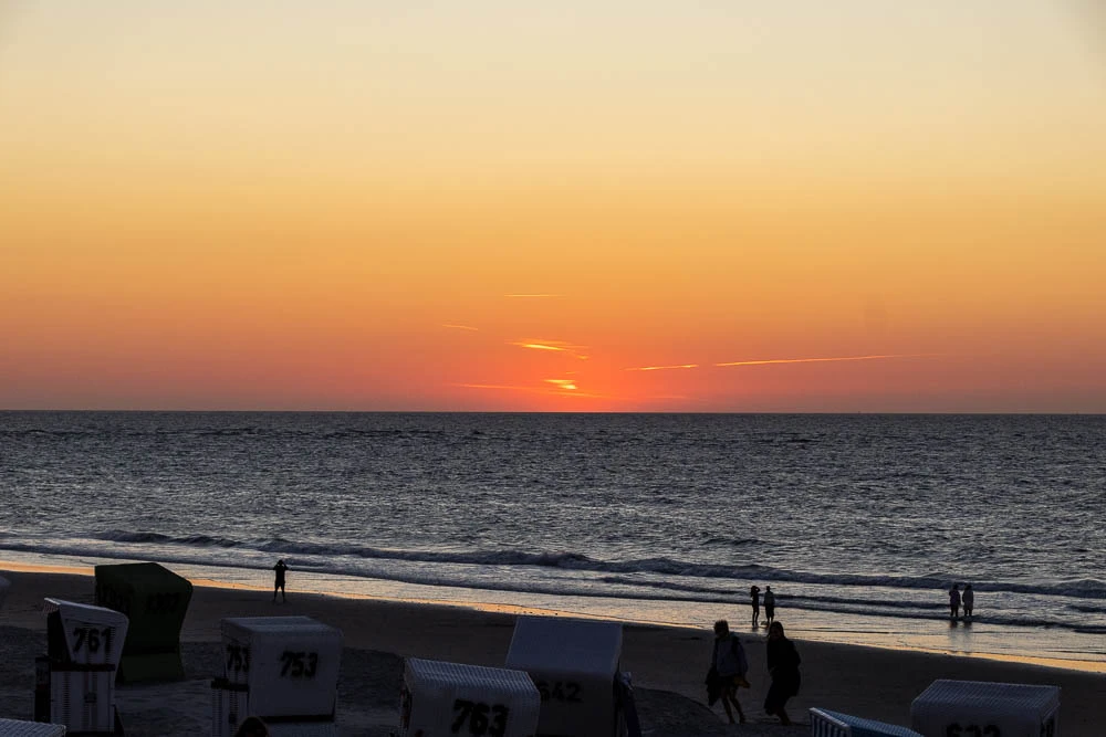 Letztes Abendlicht über der Nordsee vor Langeoog mit Strandkörben und Menschen am Strand.