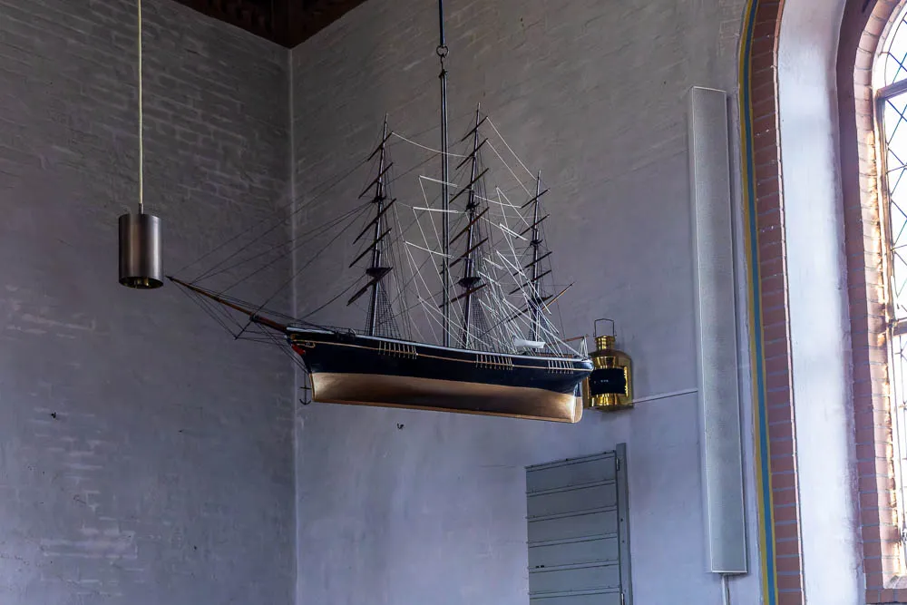 Ein detailreiches Schiffsmodell hängt im Innenraum der Inselkirche Langeoog neben einem Kirchenfenster.