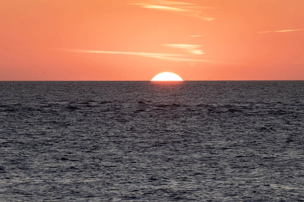 Halbe Sonne am Horizont über der Nordsee vor Langeoog unter einem orangefarbenen Abendhimmel.