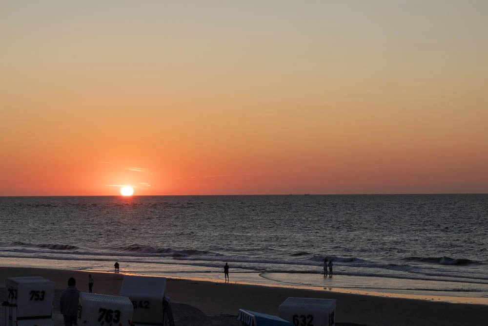 Sonne kurz über dem Horizont der Nordsee vor Langeoog mit Strand und Strandkörben im Vordergrund.