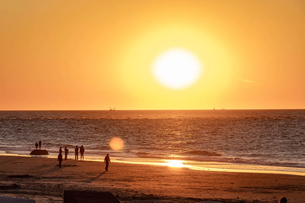 Sonnenuntergang über der Nordsee vor Langeoog mit Menschen am Strand und im Wasser.