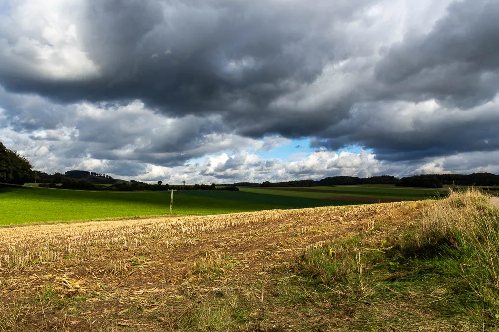 Abgeerntete Felder bei Eisborn unter einem dramatischen Himmel mit dunklen Wolken.