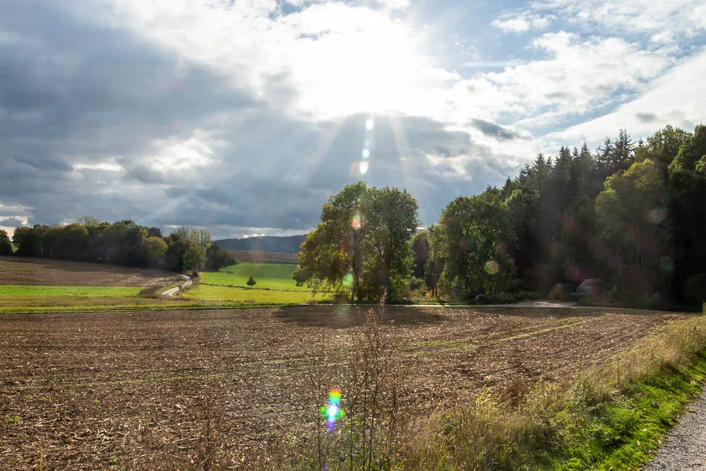 Sonnenstrahlen fallen durch die Wolken auf Felder und Wiesen bei Eisborn.