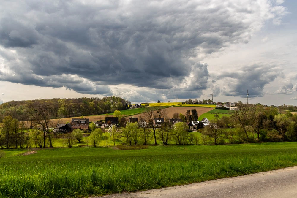 Blick vom Heinrichsknübel in Fröndenberg-Hohenheide über grüne Felder und die Ortschaft Bausenhagen unter einer dunklen, imposanten Wolkenformation.