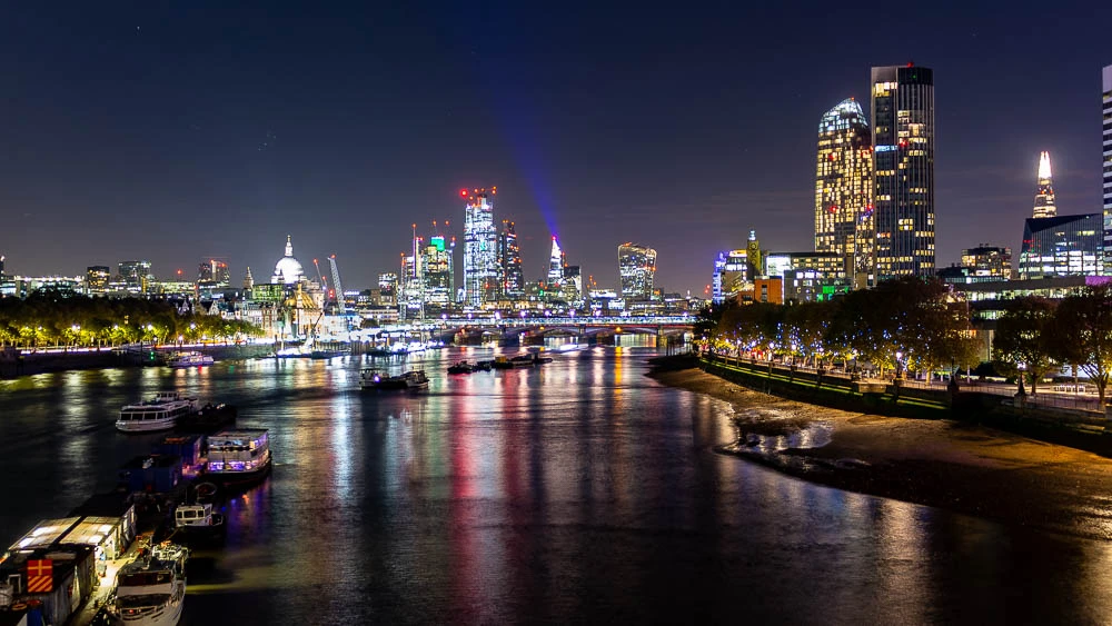 Nächtlicher Blick von der Waterloo Bridge auf die beleuchtete Skyline von London und die Spiegelungen der Gebäude in der Themse.